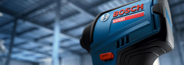 Close-up of a blue Bosch tool with a red logo, against a blurred, bright background.