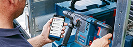 A man is using a Bosch Professional tool and holding a smartphone.