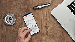 A smartphone on a wooden table, next to a laptop keyboard and a tool.