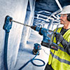 A man with a safety helmet is drilling into a wall with a blue Bosch tool.