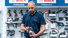 A man with a beard is holding a Bosch Professional tool in his hand.