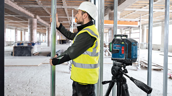 A construction worker with a helmet measures with a Bosch Professional laser in a room.