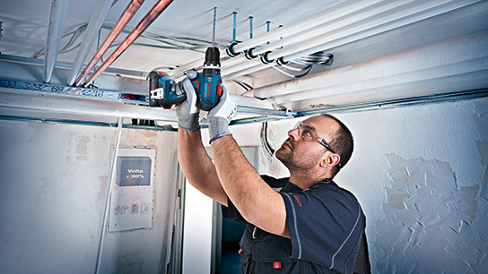 A craftsman is installing pipes with a Bosch Professional cordless screwdriver.
