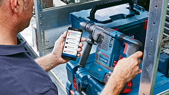 A man holds a smartphone and operates a blue Bosch Professional drill.