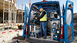 A tradesman in a safety vest stands by a blue Bosch tool cart.