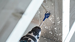 A Bosch Professional cordless drill penetrates a wall, shavings fly.