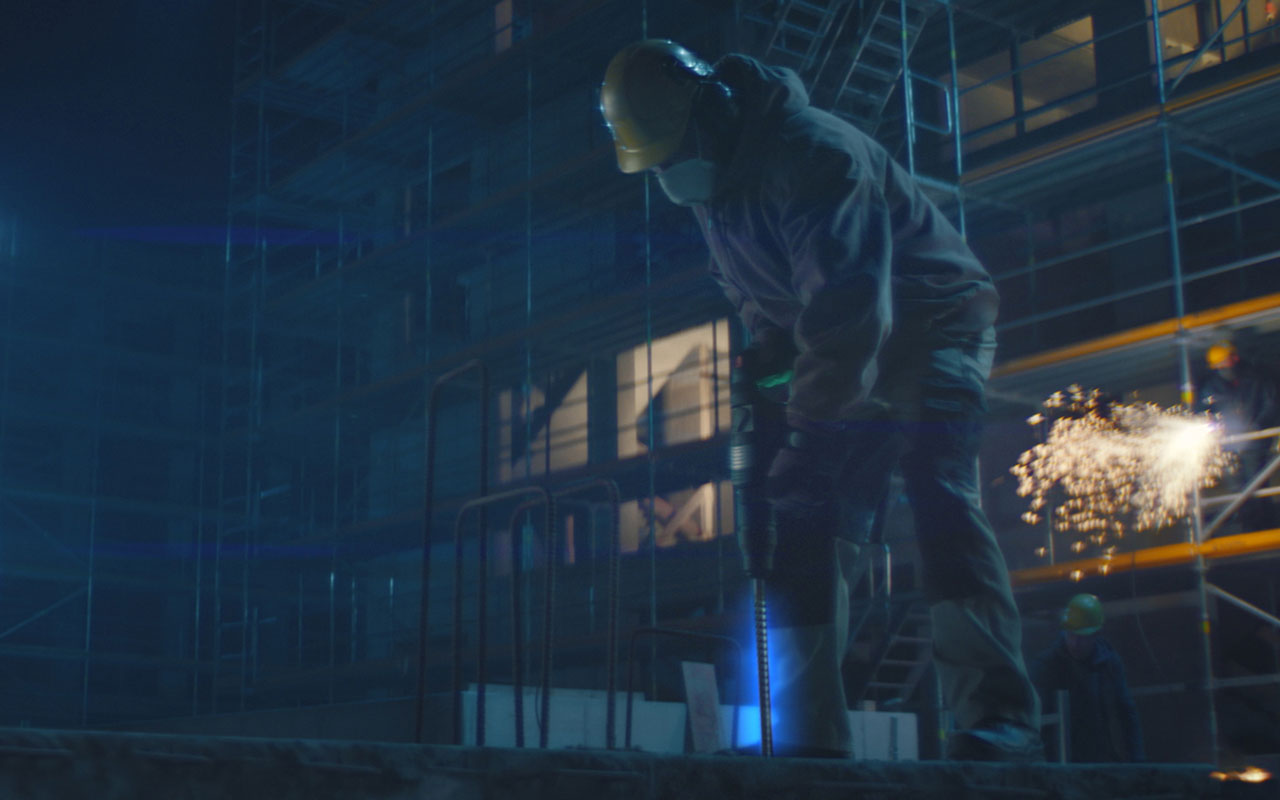 A worker with a helmet is drilling at a construction scaffold at night.