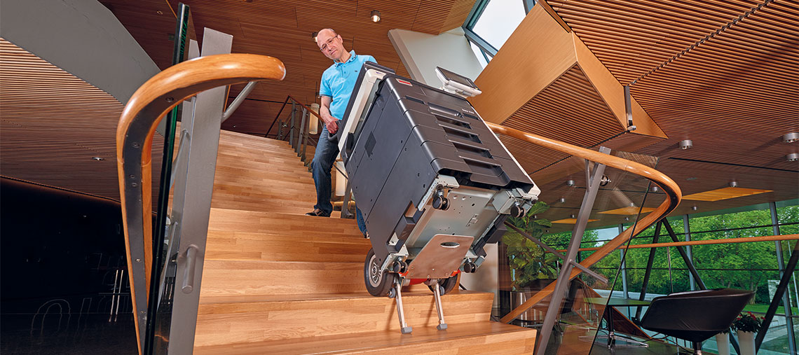 A man carries a Bosch toolbox down the stairs in a modern room.