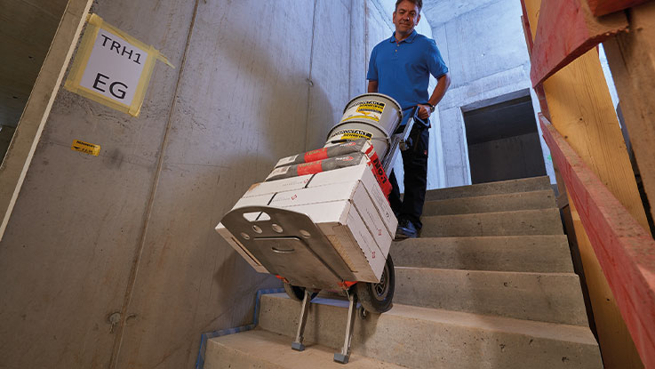 A man is carrying a hand truck with boxes down the stairs.