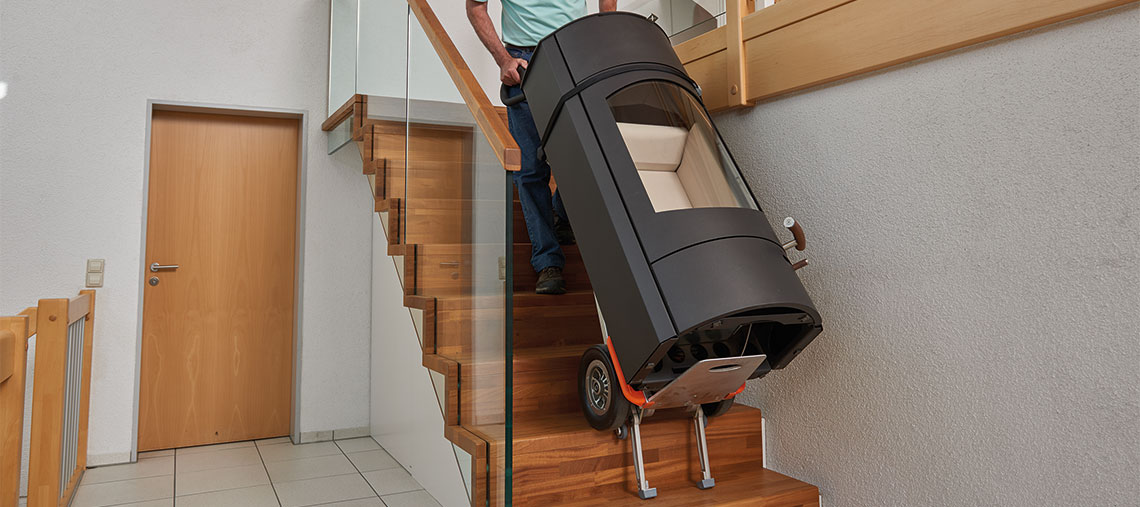 A man is carrying a black stairlift with a seat down the stairs.
