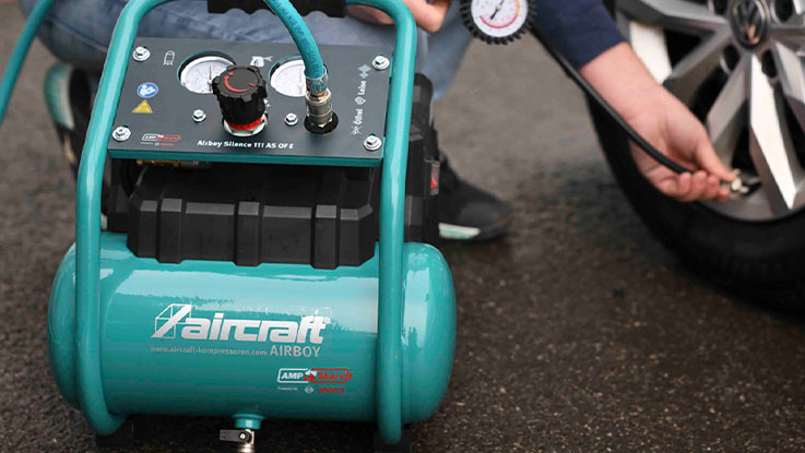 A green air compressor stands next to a driver who is inflating tires.