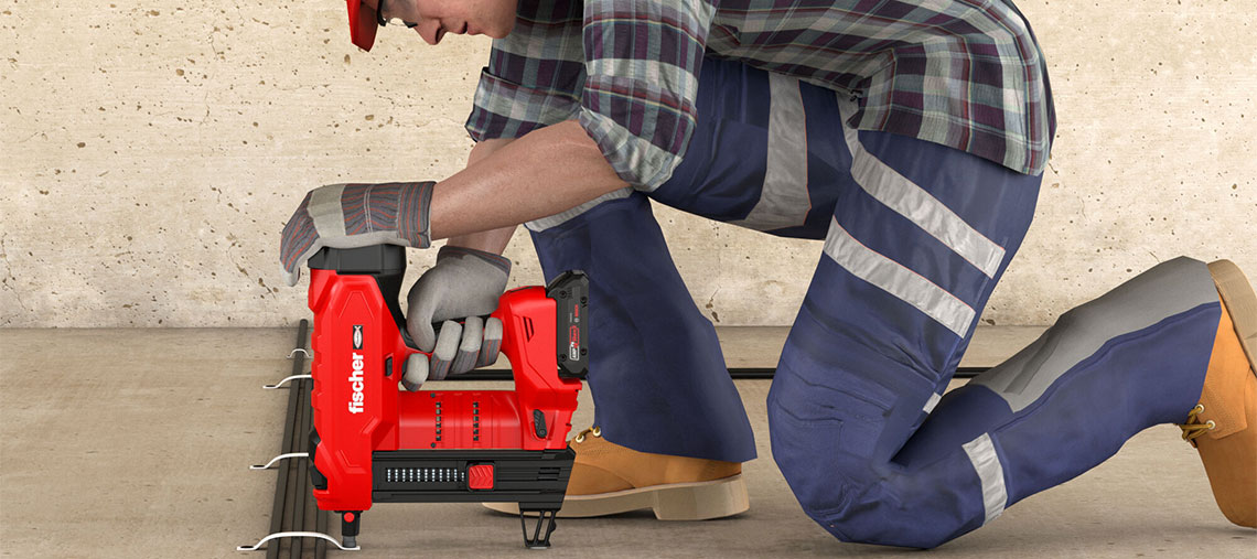A worker is using a red battery nailer on a concrete floor.