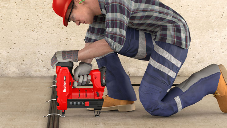 A worker is using a red battery nailer on a concrete floor.