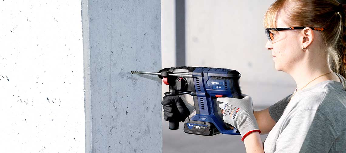 A woman is drilling into a wall with a blue Bosch Professional tool.