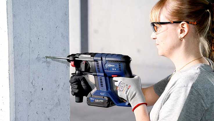 A woman wearing safety glasses is using a blue Bosch Professional drill.