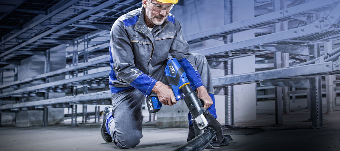A man in work clothes is using a blue Bosch Professional tool.