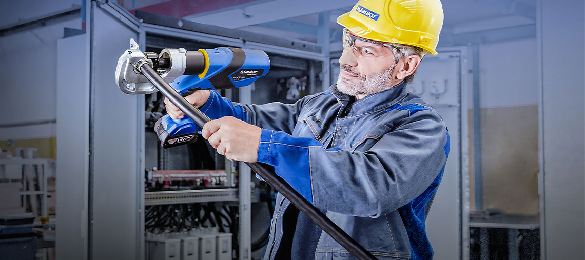 A man with a yellow helmet is using a blue tool in a workshop.