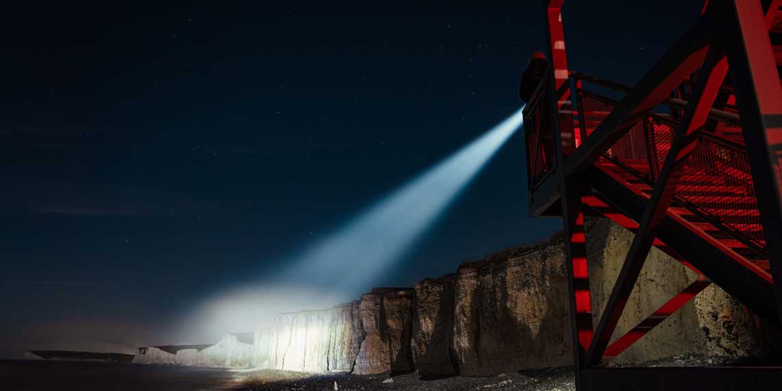 A person on a red staircase shines a flashlight on cliffs.