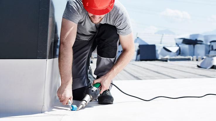 A craftsman in a red helmet is using a Bosch tool on the roof.