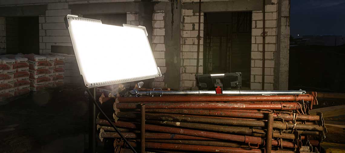 A bright construction light stands on a scaffold made of red pipes at a construction site.