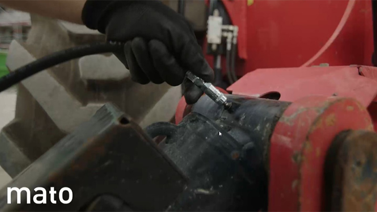 A worker wearing gloves connects a hose to a red device.