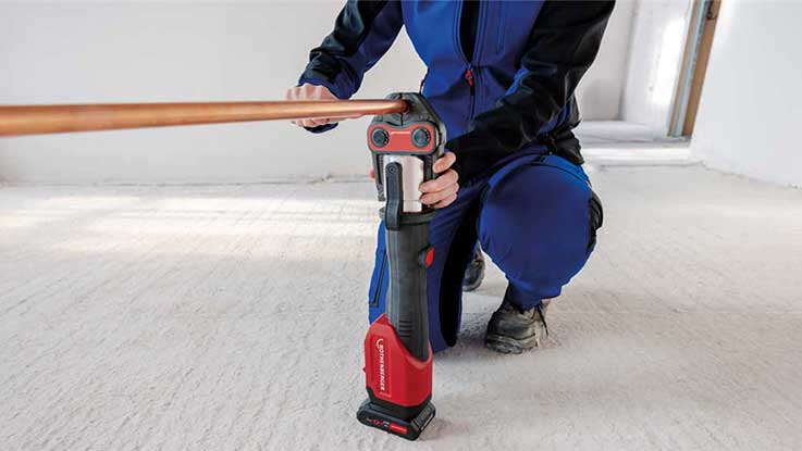 A Bosch Professional cordless tool is held against a copper pipe.