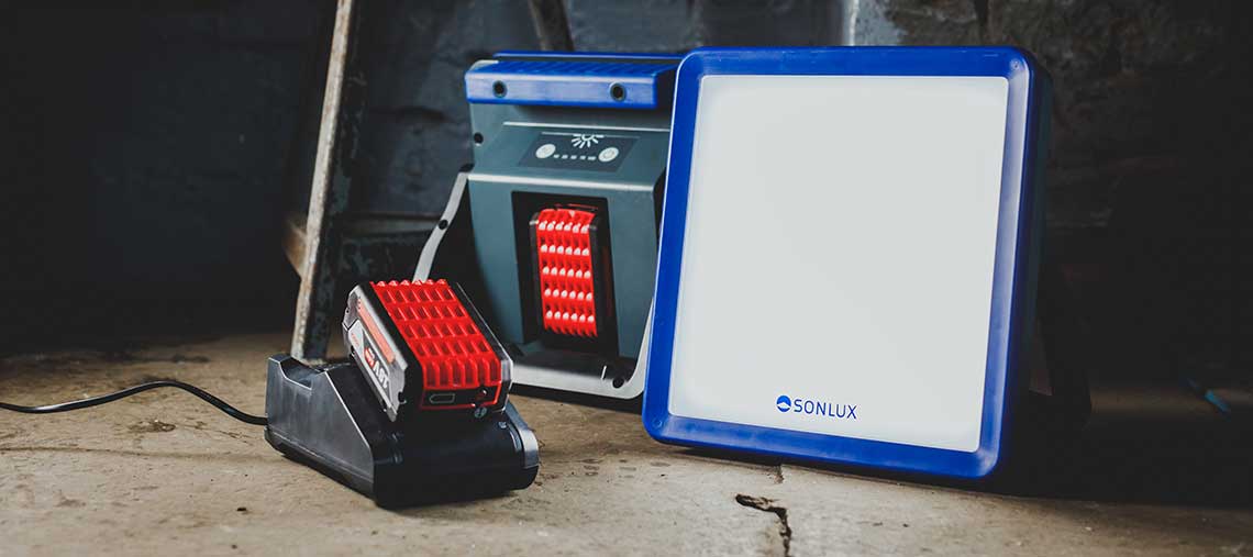 A red Bosch battery on a black charging station next to a spotlight.