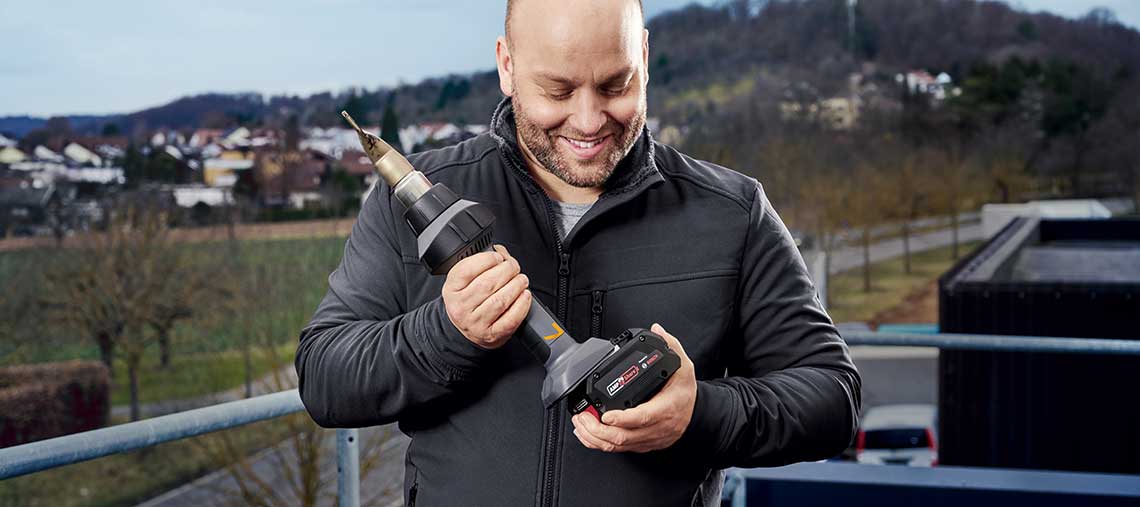 A man holds a Bosch Professional cordless screwdriver and smiles.