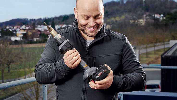 A man is holding a Bosch Professional cordless screwdriver in his hand.