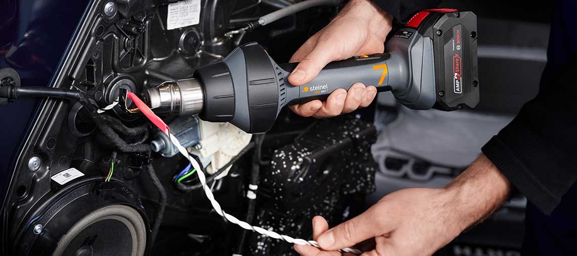 A craftsman is using a Steinel hot air gun on a cable.