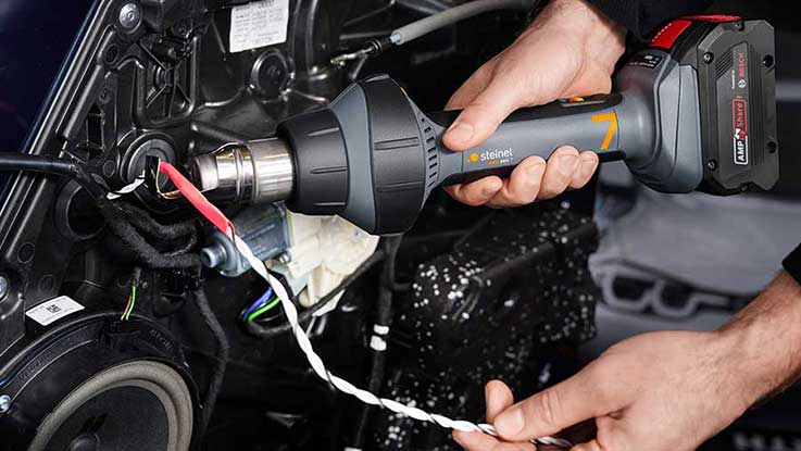 A gray hot air hairdryer is held at a cable connection.