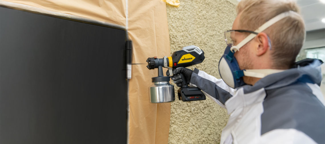 A craftsman is spraying paint on a wall with a Wagner device.