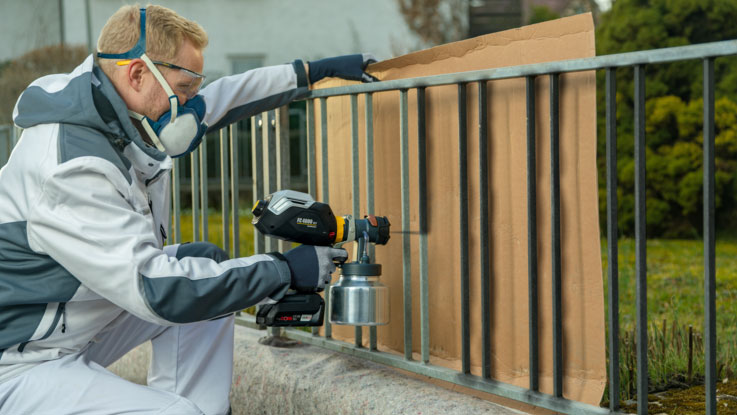 A man is spraying with a Bosch Professional paint device on a railing.