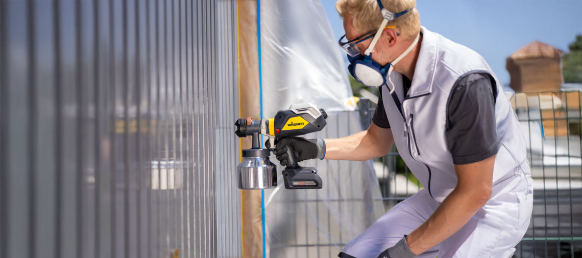 A craftsman is spraying a wall with a Wagner painting device.