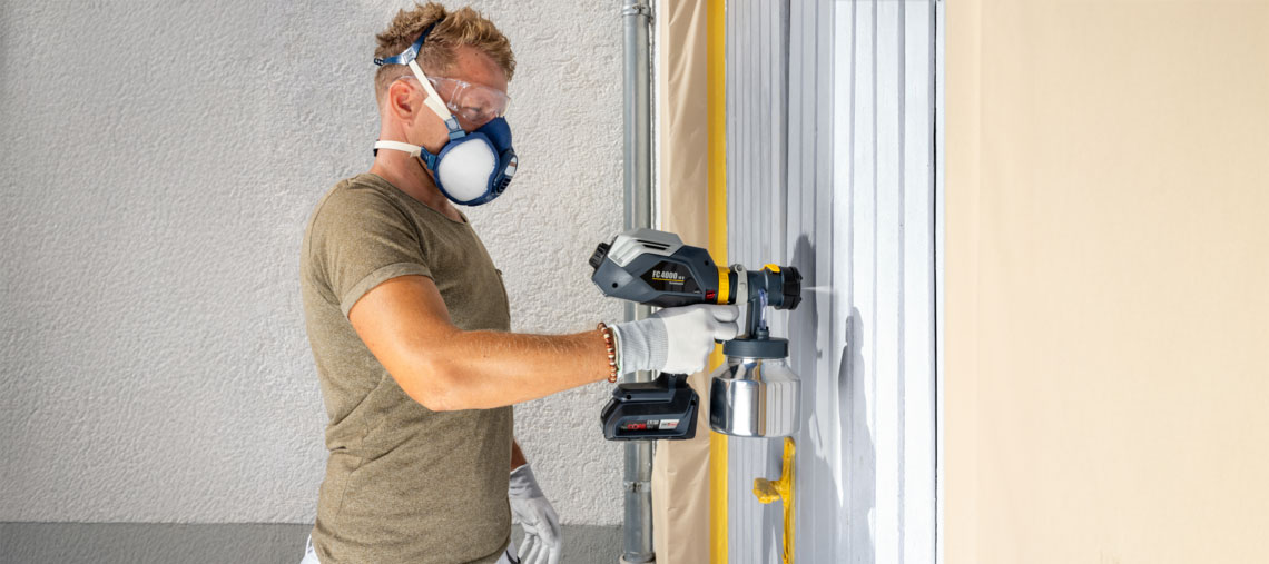 A man is spraying a wall with a Bosch Professional paint sprayer.