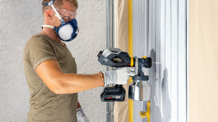 A man sprays paint with a Bosch Professional Sprayer on a wall.