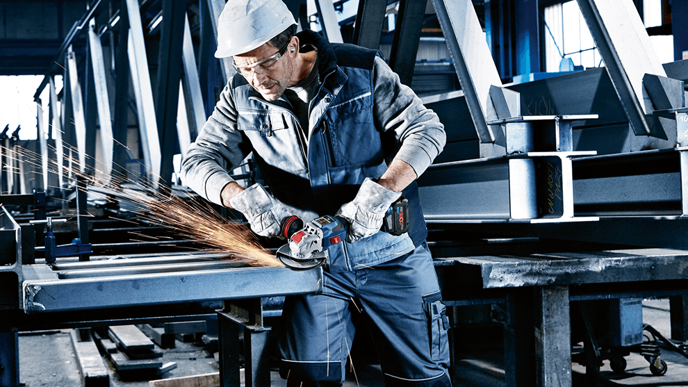 A worker with a Bosch angle grinder is processing metal parts in a workshop.
