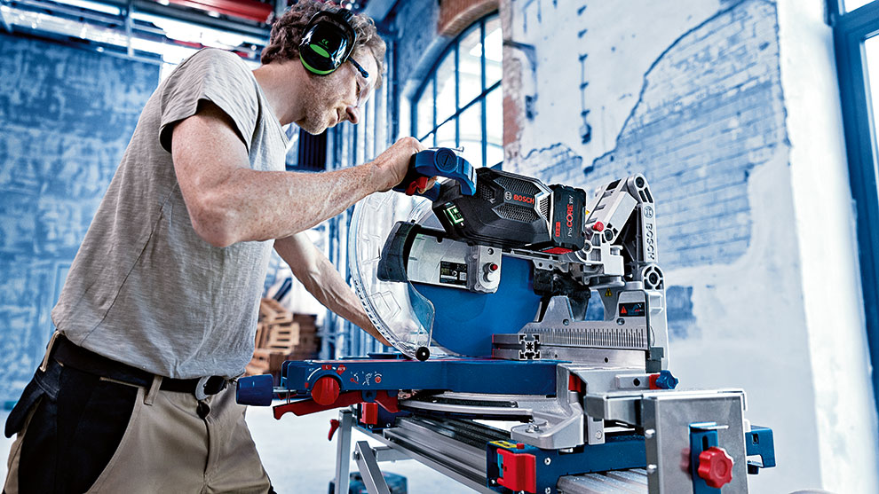 A man is using a Bosch Professional miter saw in a workshop.