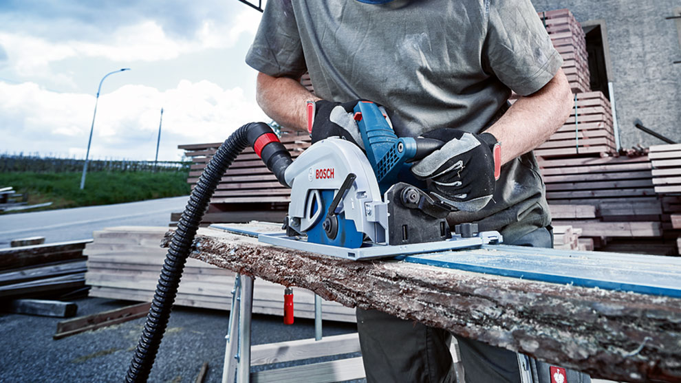 A man is using a Bosch Professional circular saw on a wooden log.