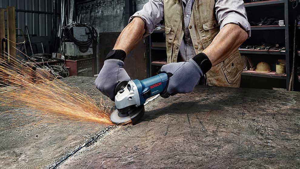 A craftsman is using a blue Bosch Professional angle grinder on a table.