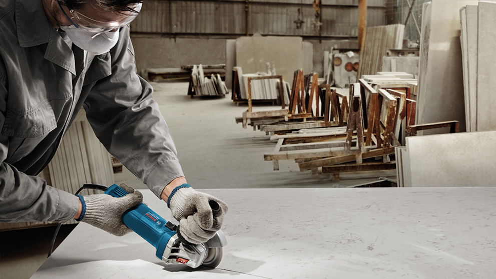 A worker is using a blue Bosch Professional angle grinder.