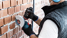 A craftsman is using a Bosch Professional angle grinder on a wall.