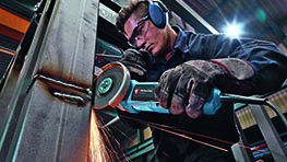 A craftsman wearing safety glasses and headphones is grinding metal.