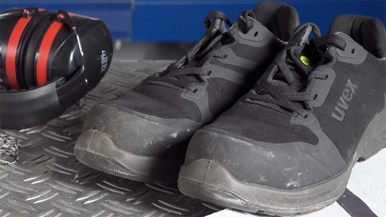 Black Uvex safety shoes are lying on a metal surface.