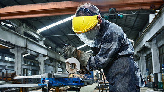 A worker with a yellow helmet is cutting metal in a workshop.