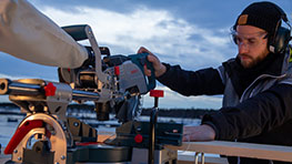 A man wearing hearing protection is using a Bosch Professional miter saw outdoors.