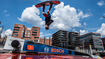 A wakeboarder jumps over a ramp with the Bosch logo in sunny weather.