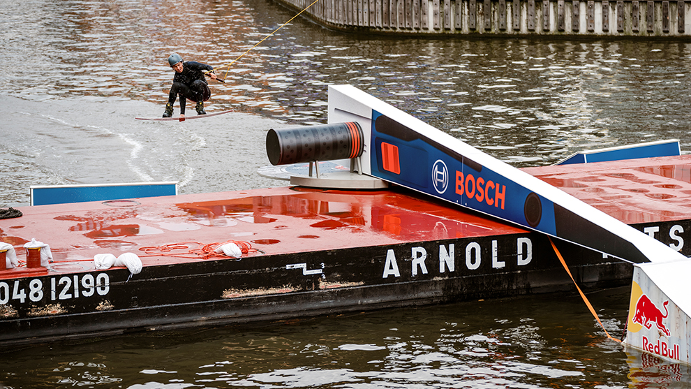 A wakeboarder is riding on a body of water next to a red Bosch boat.