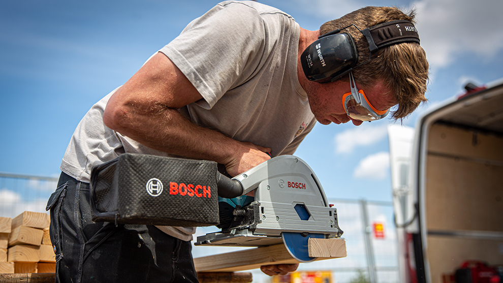 A craftsman is cutting wood with a blue Bosch Professional saw.