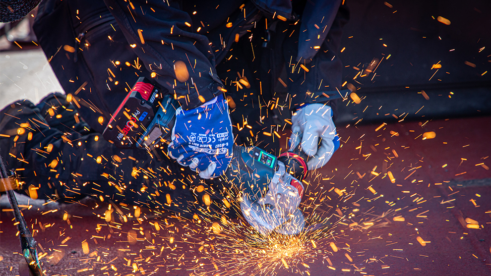 A person is cutting metal with a Bosch tool, sparks are flying.